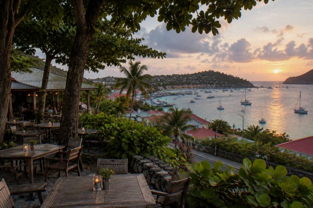 An empty restaurant terrace at dusk overlooking a harbour with lights on the water