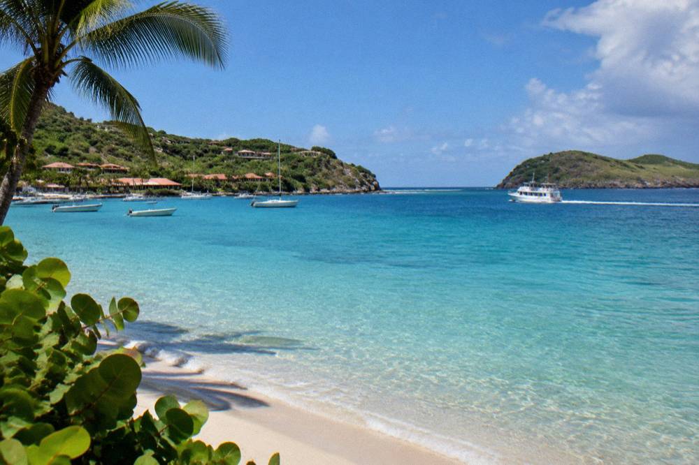 A small white ferry boat crossing open blue Caribbean water toward a green island