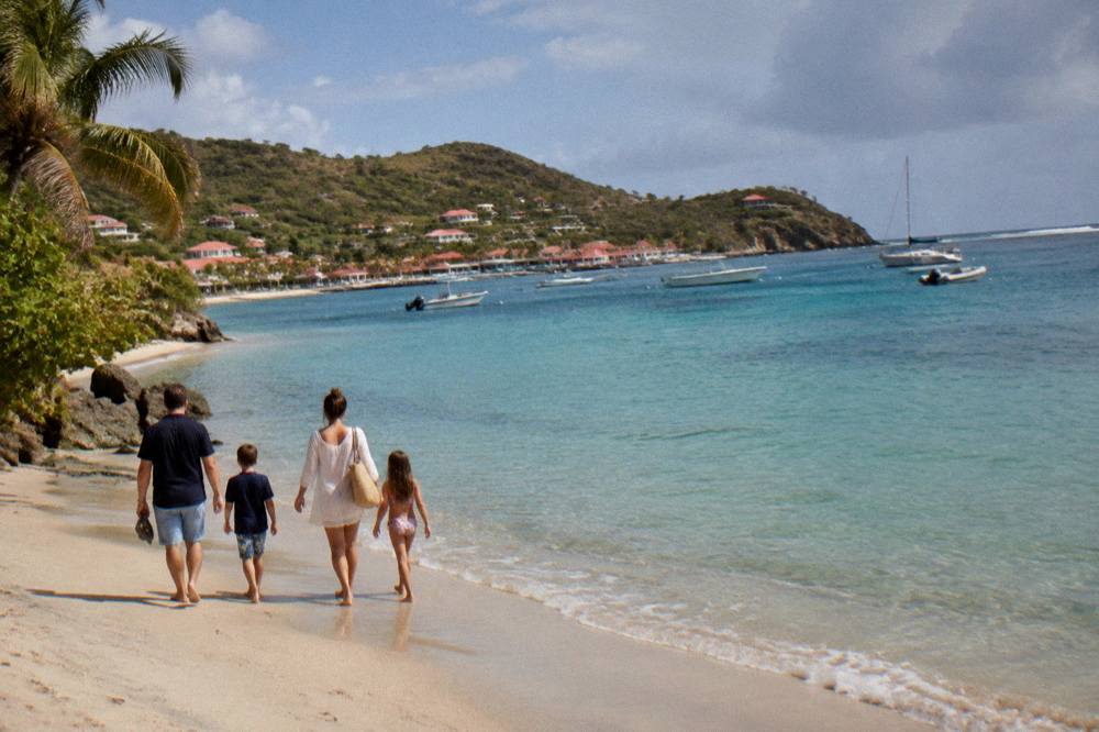 A family of four walking along the water's edge of a quiet Caribbean beach in late afternoon light