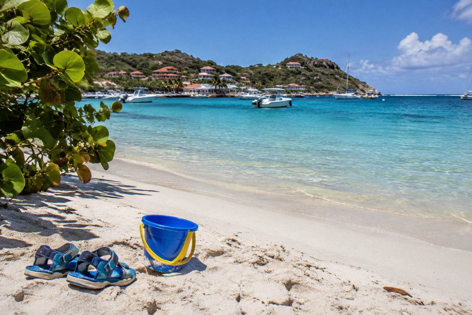 Children's sandals and a bucket on pale beach sand, no people