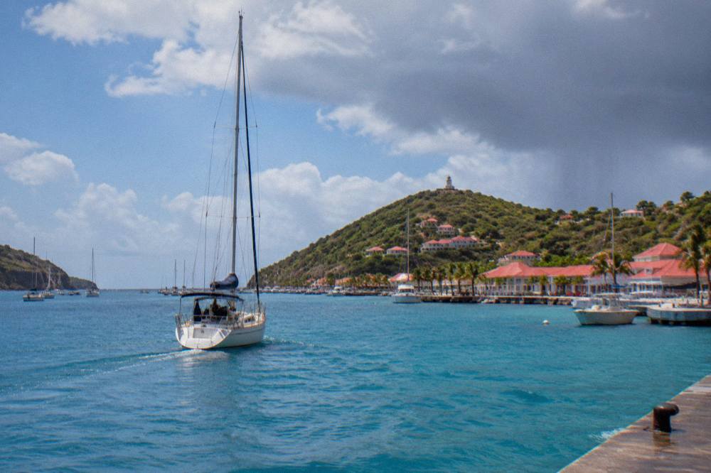 A sailing yacht motoring toward the entrance of Gustavia harbor at midday