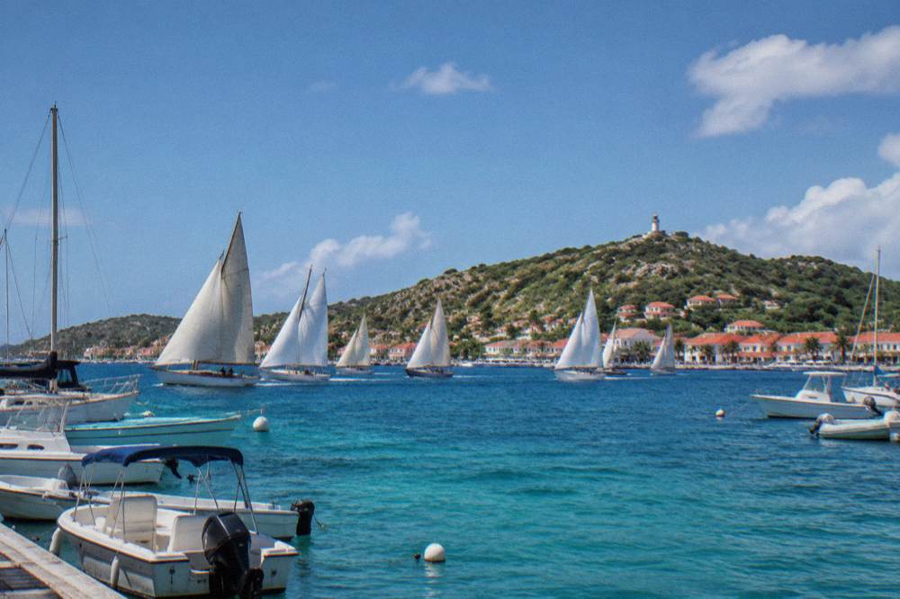 A line of classic sailing yachts racing outside Gustavia harbor