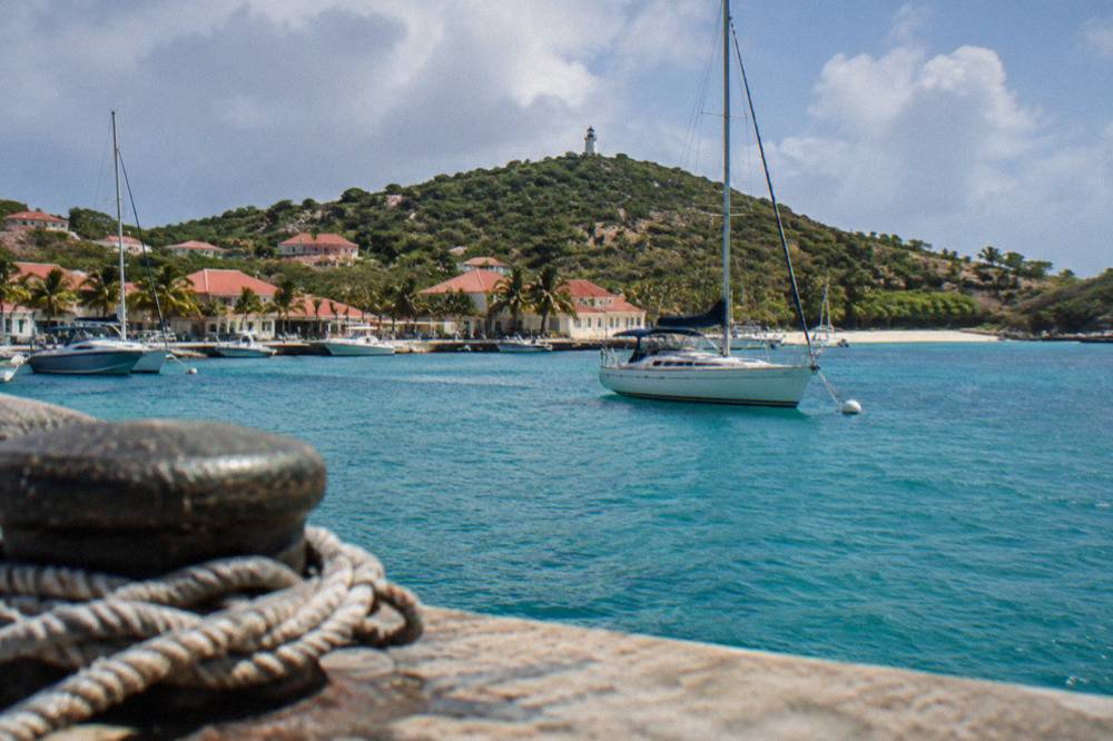 A yacht on a mooring buoy in a green hillside bay with a sandy beach at its head