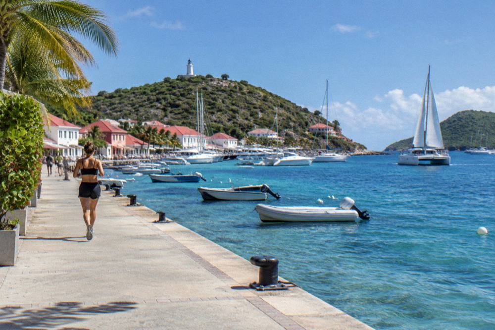 A catamaran under sail on open water between two green islands