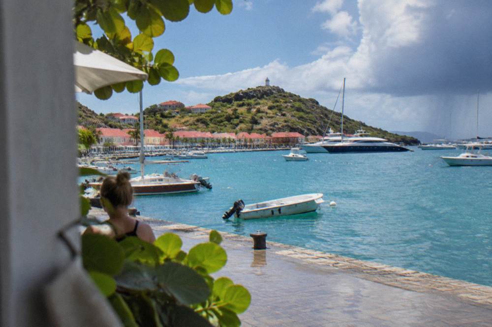 A red-roofed Caribbean harbour town wrapped around a bay of moored yachts