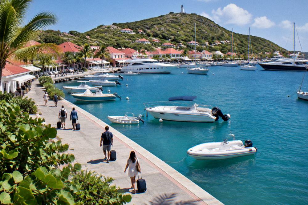 Travellers with rolling bags walking along a sunny Caribbean waterfront promenade