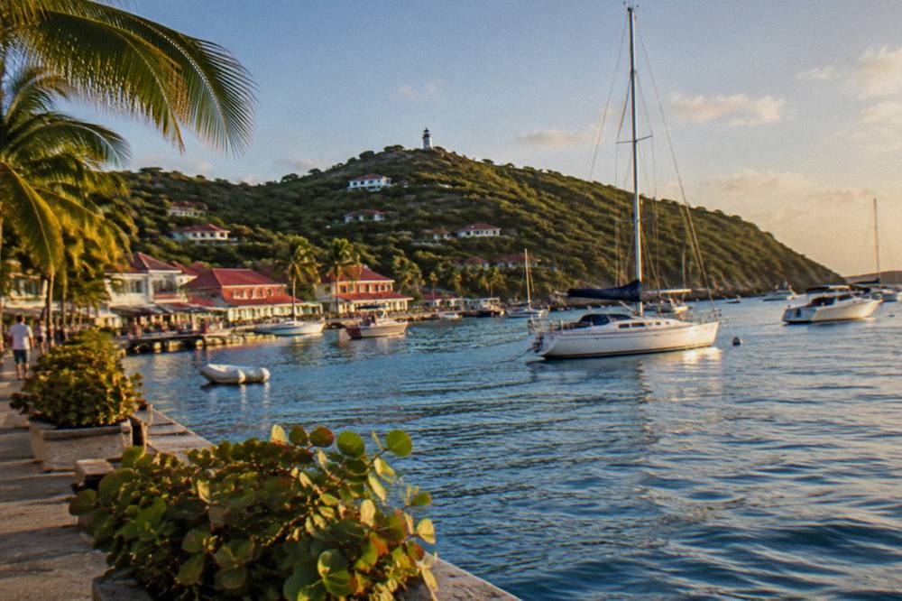 A sailboat anchored in a quiet bay with a wooded hill behind it