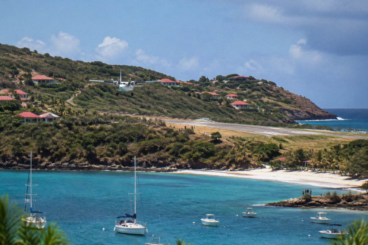 A small turboprop aircraft on a Caribbean island airstrip between green hills and blue sea