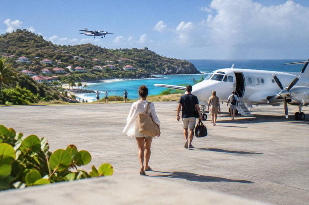 Passengers walking across a sunny apron toward a small white turboprop airplane