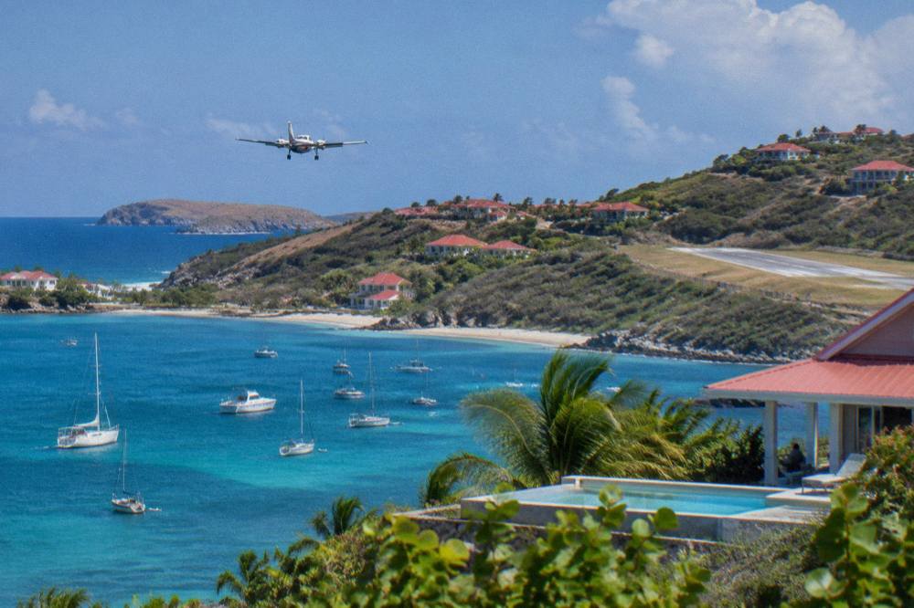 A hillside villa with a pool overlooking a turquoise bay dotted with boats