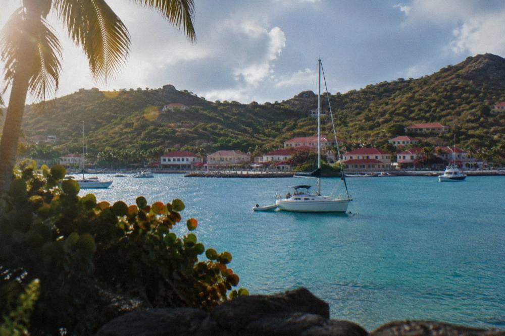 A sailboat moored in a quiet turquoise bay with a wooded headland behind