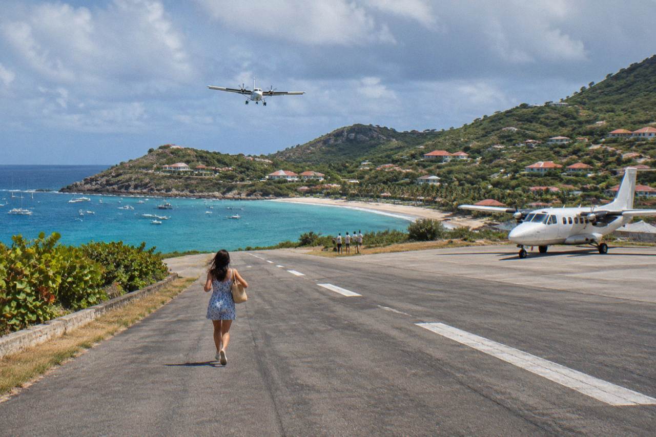 A small twin-engine turboprop aircraft parked on a Caribbean island airstrip with green hills behind it