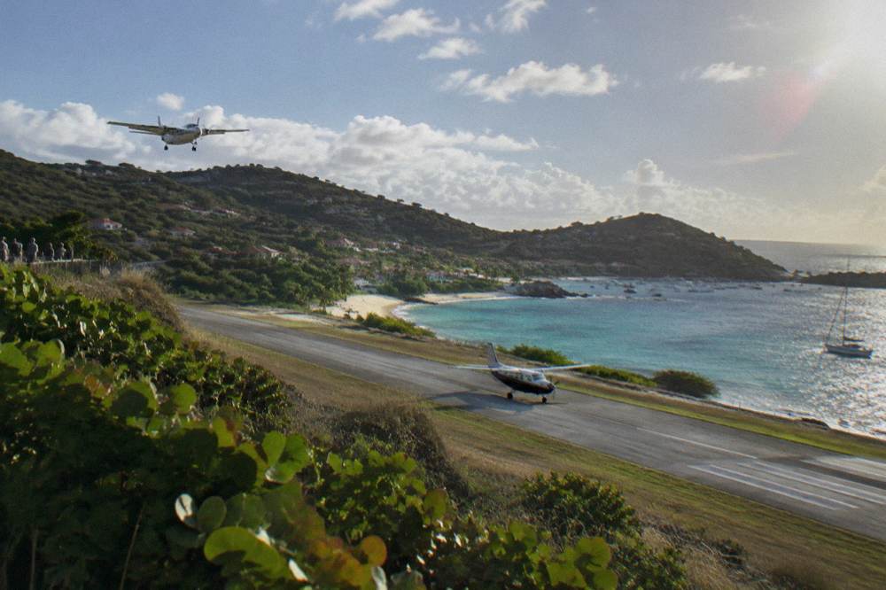 A single-engine turboprop taxiing on a narrow Caribbean airstrip between green hills