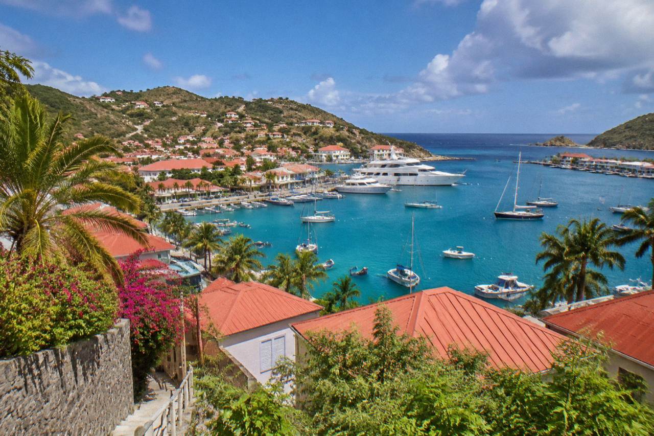 A view over red rooftops and a small harbor with turquoise water and green hills