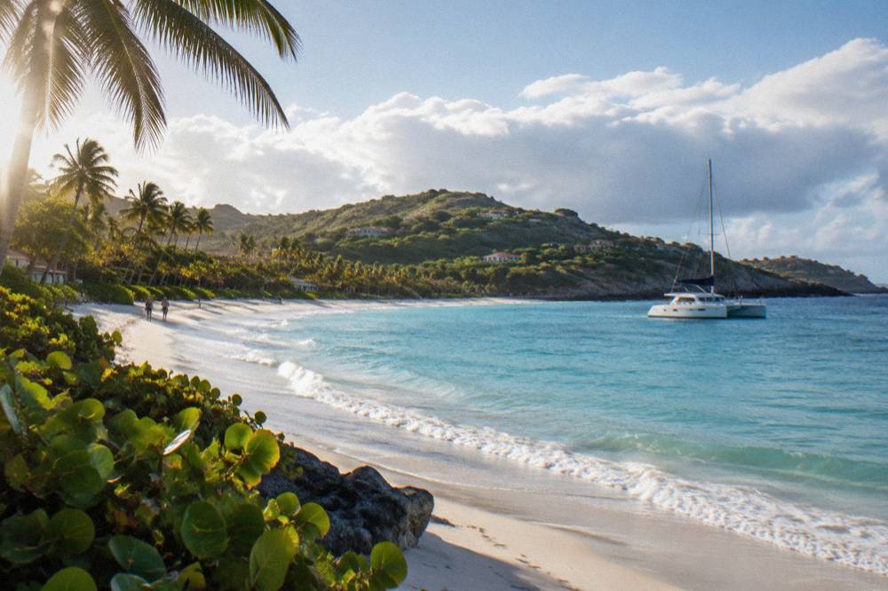 A sailing catamaran anchored in a quiet bay with green hills behind it