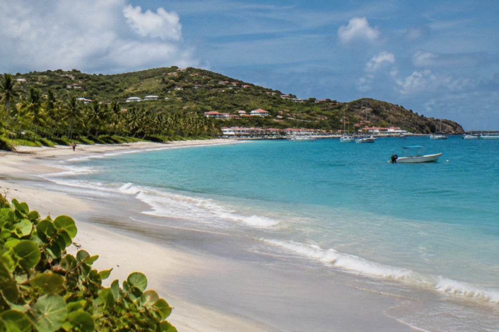 A wide crescent of pale sand between green hills and calm blue sea