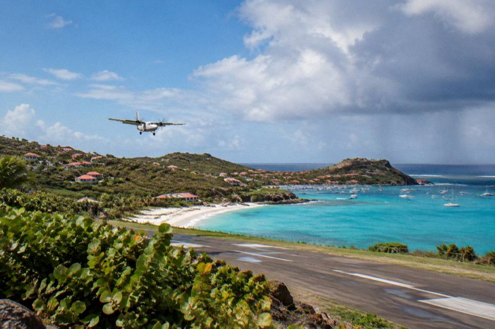 A small turboprop aircraft on a short runway beside a Caribbean beach