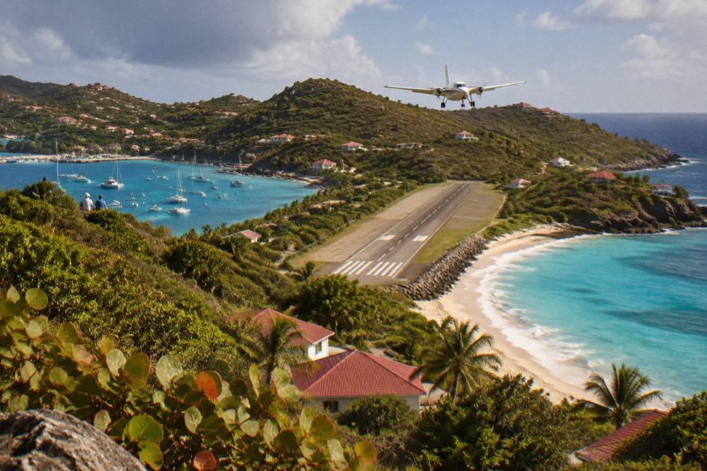 A small turboprop aircraft on a short runway beside a beach and hills