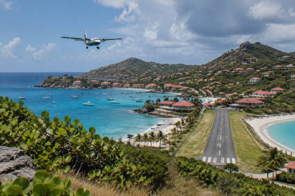 A small turboprop aircraft on a short runway beside a beach and hills