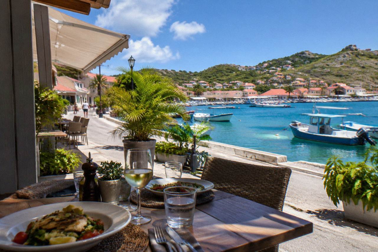A table set for lunch on a terrace above a Caribbean harbor with fishing boats in the water below