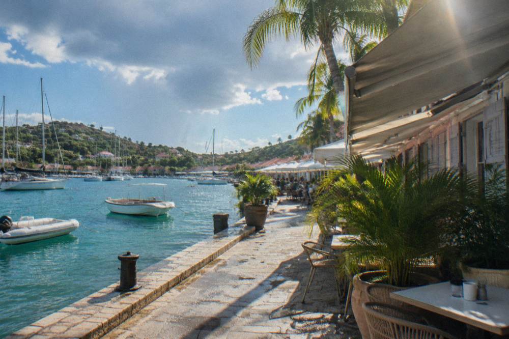 Sailboats moored in a harbor with diners at outdoor tables along the waterfront