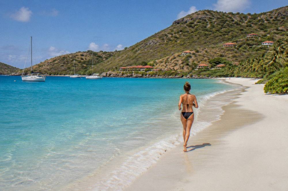 An empty curve of pale sand meeting clear shallow water with hills at each end