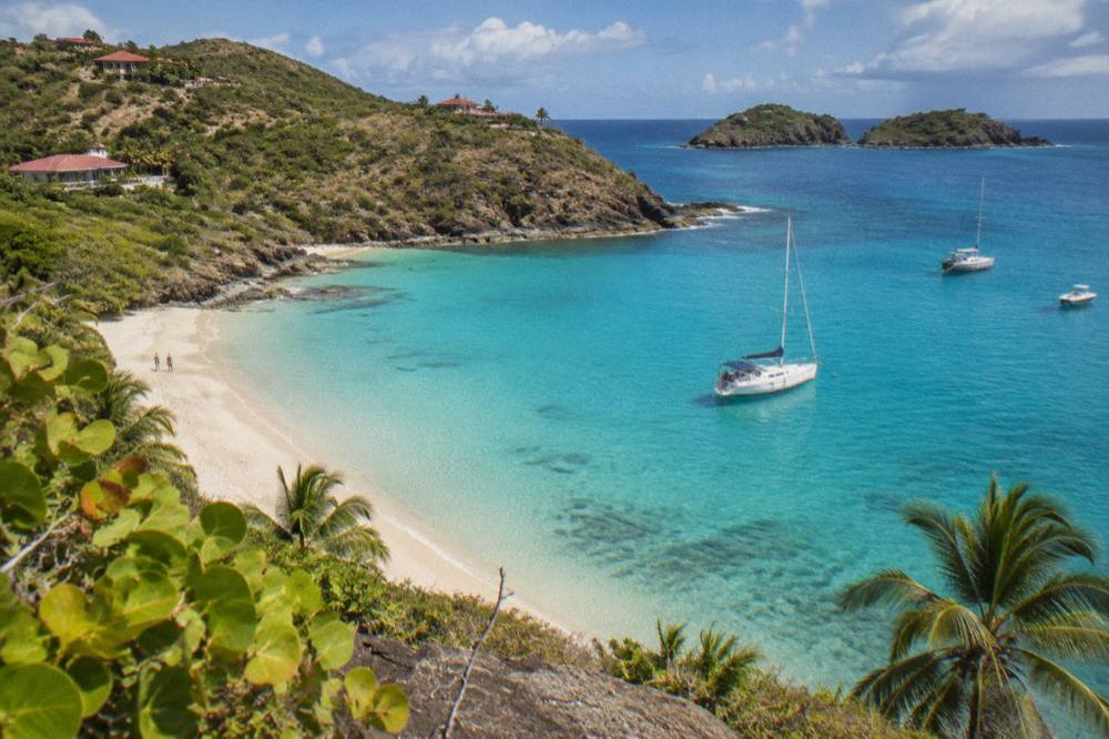 A sailboat anchored in a clear bay with rocky green islands beyond