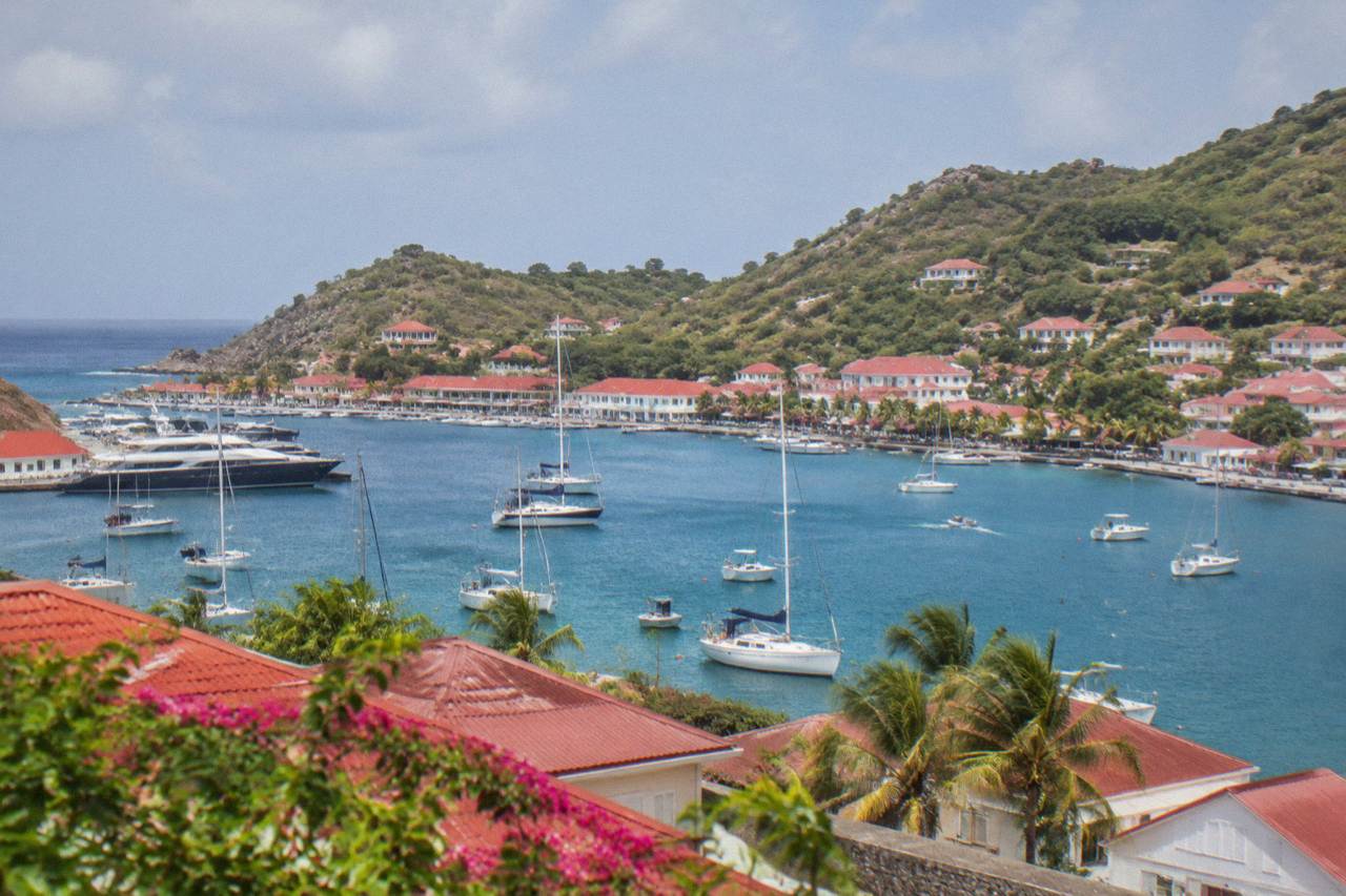A view over red rooftops and sailboats anchored in a Caribbean harbour below green hills