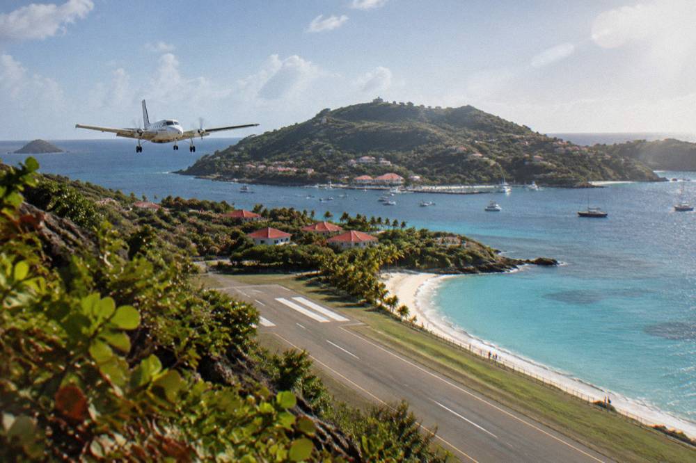 A small white turboprop aircraft on a short runway beside a beach and hills