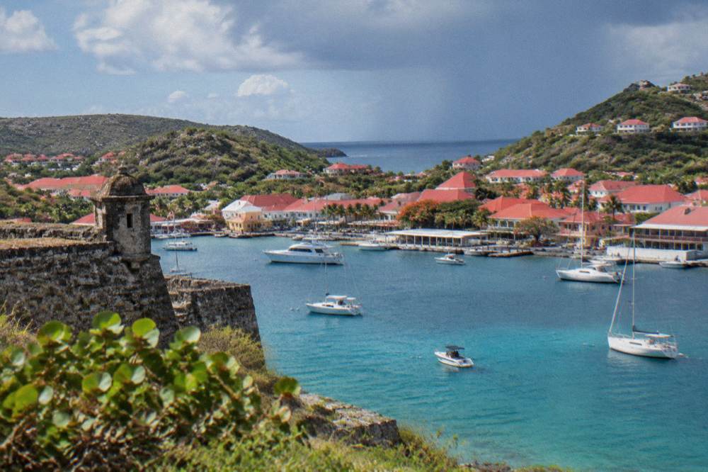 A stone fort ruin overlooking a harbour with boats and hills beyond