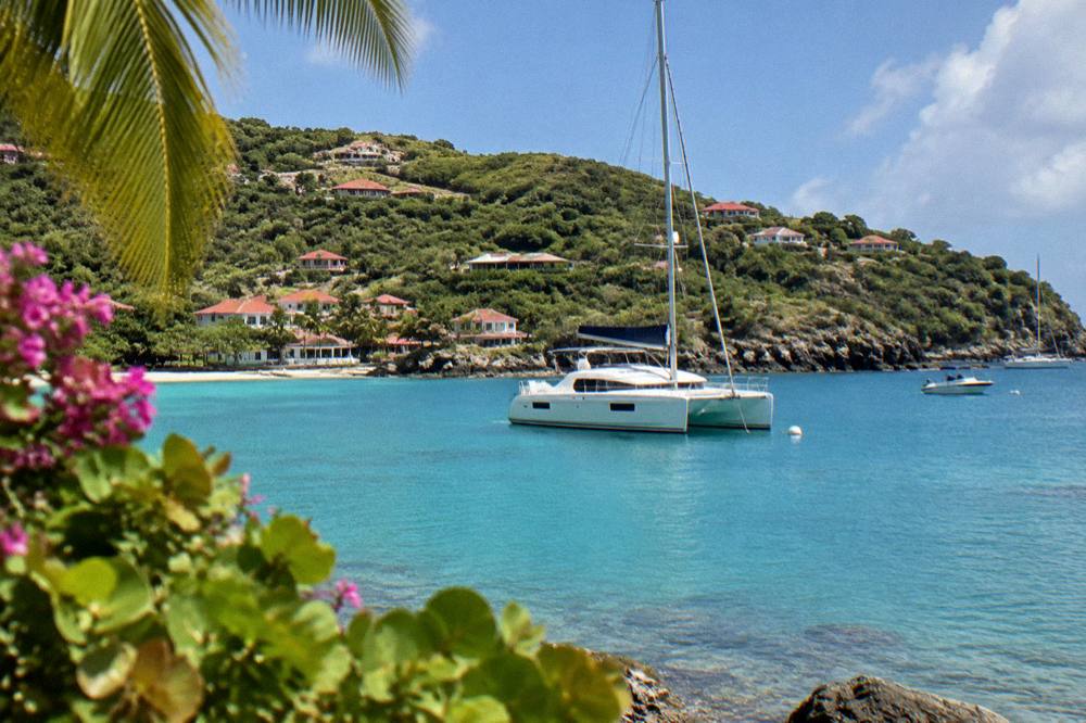 A sailing catamaran anchored in a quiet bay with a wooded headland behind it