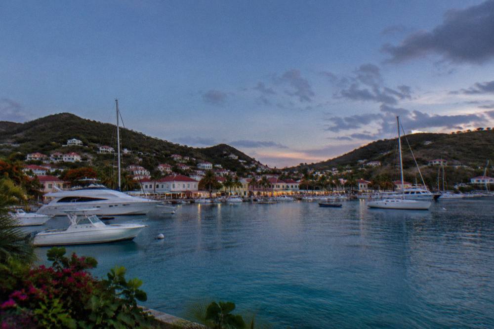 White yachts moored in a small harbour with pastel buildings along the quay