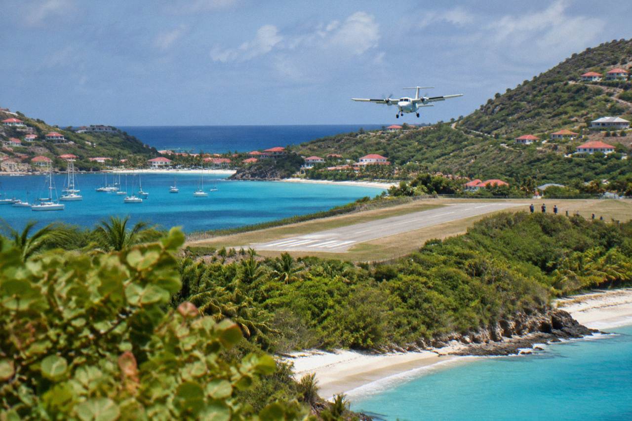 Small turboprop aircraft on a short runway between green hills and turquoise Caribbean water