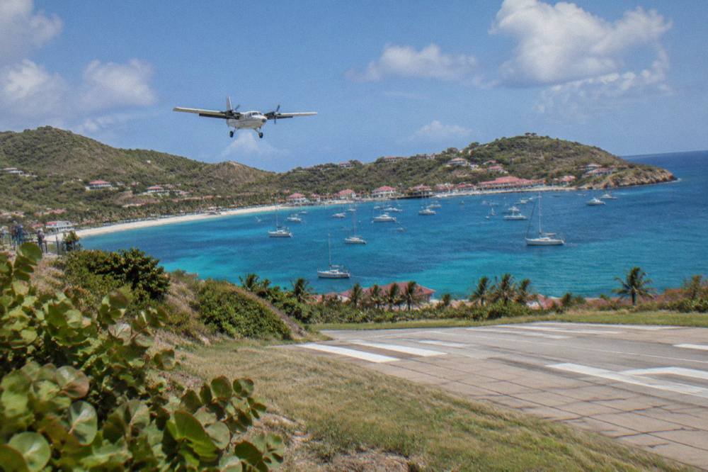 Sailing boats anchored in a wide bay with green hills rising behind a pale beach
