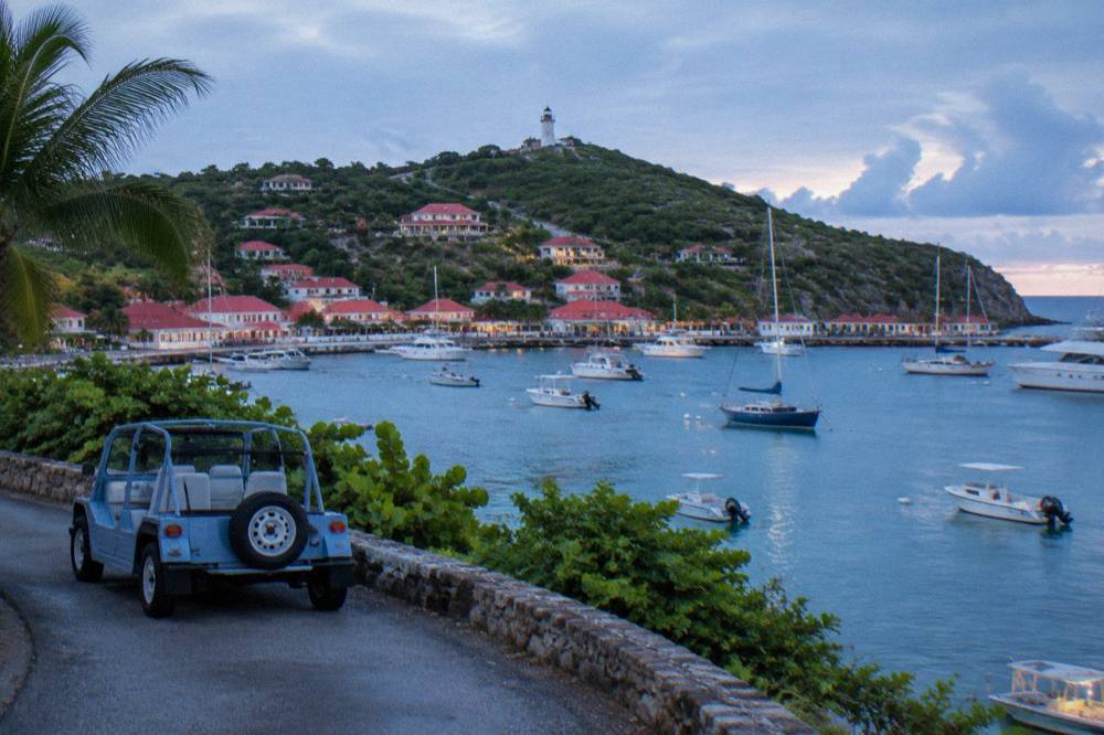 An open-air Mini Moke parked beside a narrow winding road above the sea