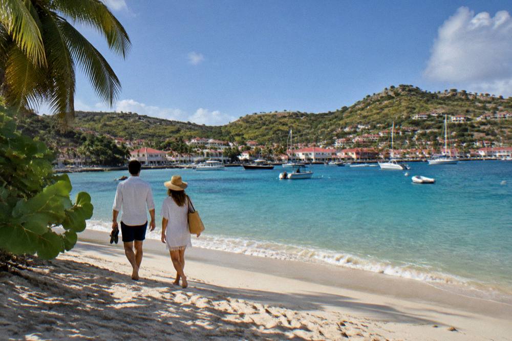 Couple walking on pale sand toward calm clear water at a St Barts beach