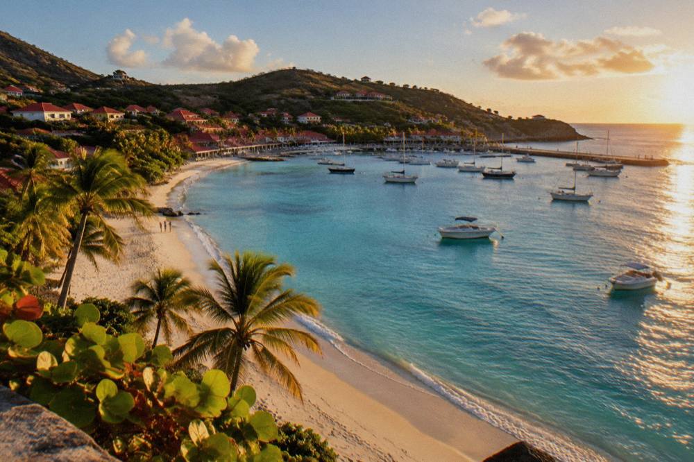 Early sun rising over a calm bay with a long sandy beach and palm trees